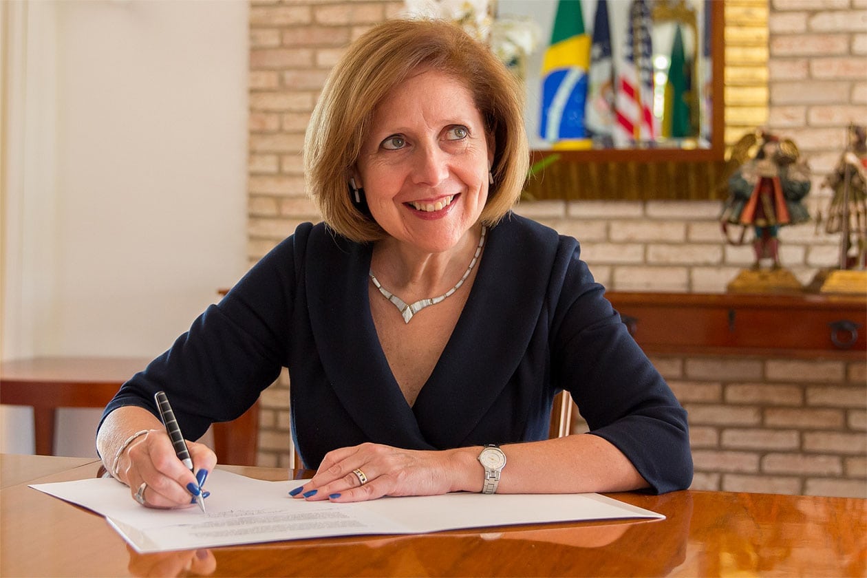 Liliana Ayalde, U.S. Ambassador to Brazil, smiles and signs document.