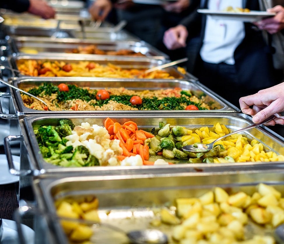 Dining hall buffet with assortment of vegetables and noodles.